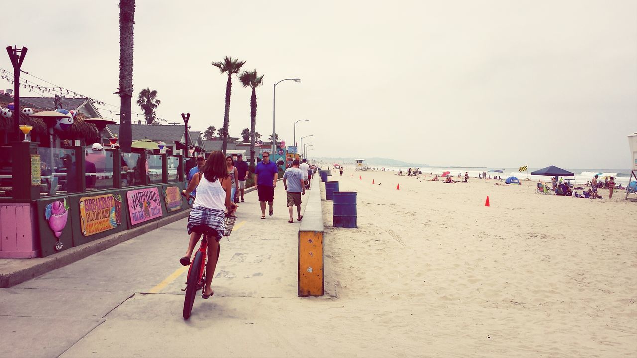 lifestyles, leisure activity, person, beach, men, full length, built structure, clear sky, building exterior, walking, large group of people, architecture, sky, casual clothing, day, sand, sea, outdoors, standing