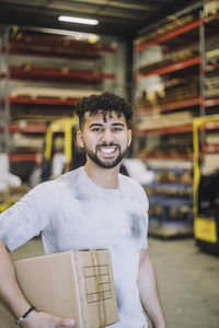 Portrait of happy young male carpenter with cardboard in warehouse