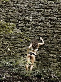 Rear view of woman in lingerie against stone wall