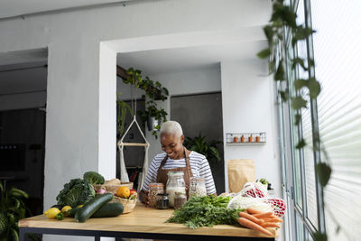 Woman with apron in kitchen , unpacking freshly bought organic fruit and vegetables