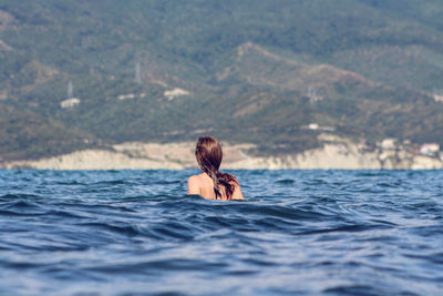 Rear view of young woman in sea against sky