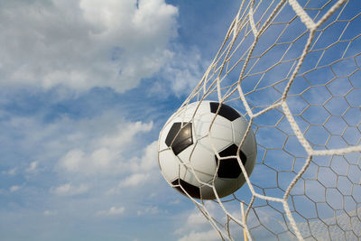 Low angle view of soccer ball in net against sky