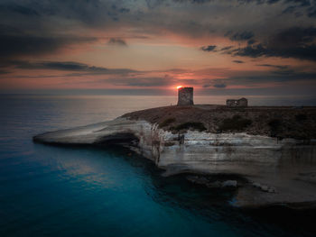 Lighthouse by sea against sky during sunset