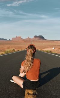 Rear view of woman sitting on road against sky