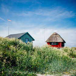 Grass growing outside huts at beach against sky
