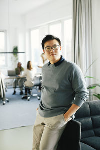 Portrait of businessman with hands in pockets leaning on sofa at office