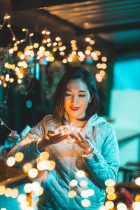 Young woman holding illuminated lighting equipment at night