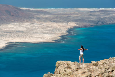 Man standing on rock by sea against mountain