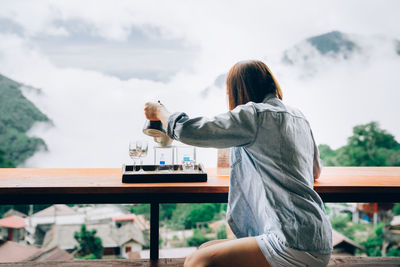 Rear view of woman sitting at table against sky