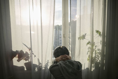 Rear view of person looking through window