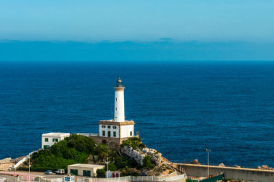 Lighthouse by sea against clear blue sky