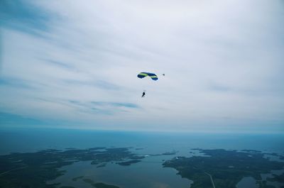 Person paragliding over sea against cloudy sky