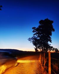 Trees on landscape against clear blue sky during sunset