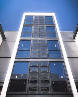 Low angle view of glass building against clear blue sky