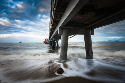 Bridge over sea against cloudy sky