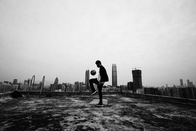 Side view of man playing with soccer ball on building terrace