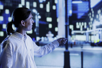 Side view of woman standing against illuminated city at night