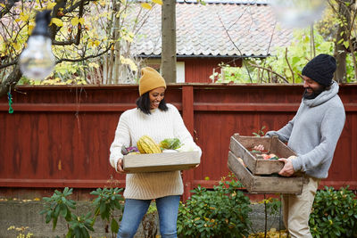 Smiling man and woman standing with fresh vegetable basket in yard