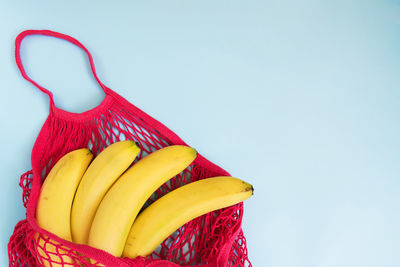 Organic banana in mesh string bag on pastel blue paper background. zero waste, minimalims, pop-art