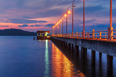 Illuminated pier over lake against sky during sunset