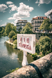 Information sign by river in city against sky