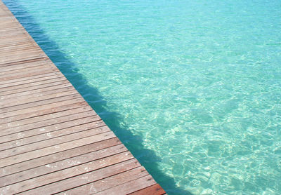 Wooden bridge crossing turquoise sea.