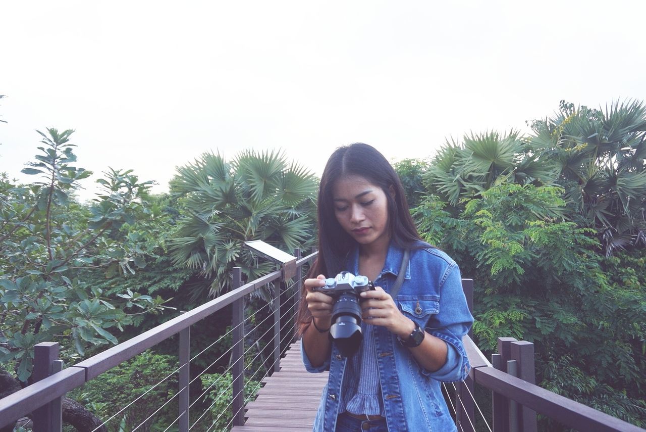 PORTRAIT OF YOUNG WOMAN PHOTOGRAPHING AGAINST SKY