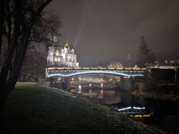 Illuminated bridge by buildings against sky at night