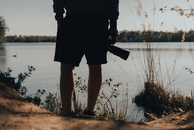Low section of man standing at lakeshore