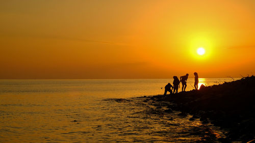 Silhouette people on sea against sky during sunset