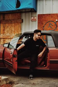 Young man sitting in car with door open on road