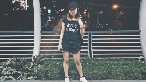 Portrait of young woman standing against illuminated road