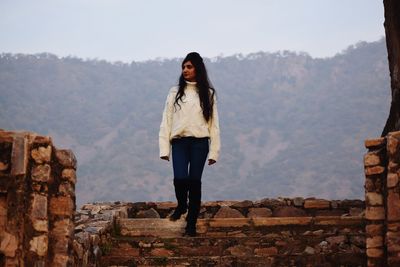 Portrait of young woman standing on mountain against sky