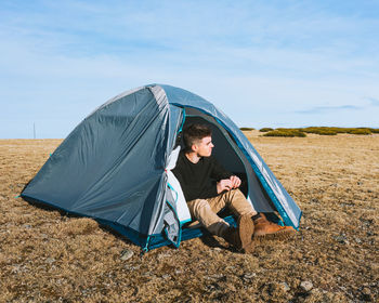 Man sitting in tent on field against sky