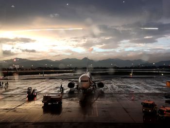 Airplane at airport runway against sky during sunset