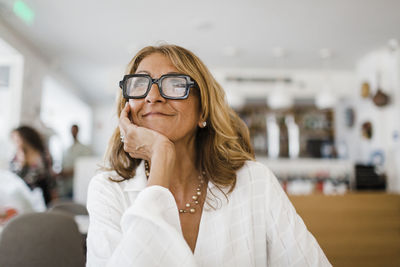 Thoughtful mature businesswoman with hand on chin sitting in restaurant