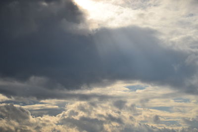 Low angle view of sunlight streaming through clouds