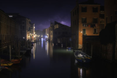 Canal amidst buildings in city at night