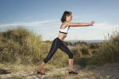 Fit woman doing arm and body stretches outdoors in sand dunes