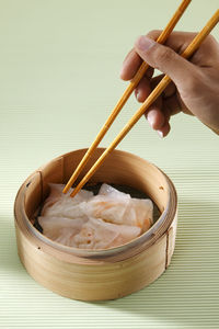 Close-up of hand having dim sum in container with chopsticks on table