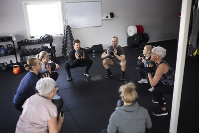 High angle view of people exercising with kettlebells while squatting in gym