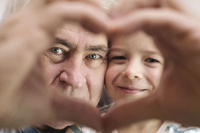 Grandfather and grandson making a heart shape hand gesture together, looking at camera. happy old