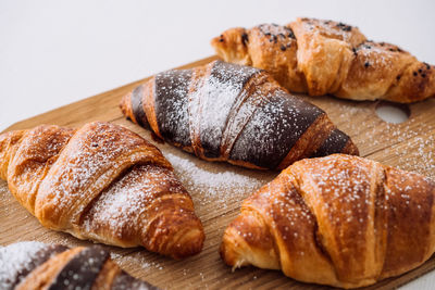 Close up bunch of appetizing brown and chocolate croissants with powdered sugar on a wooden board