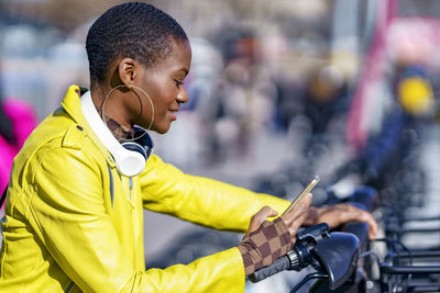 Woman with smart phone renting bicycle at parking station