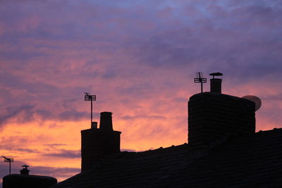 Smoke stacks of house against cloudy sky during sunset