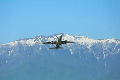 Low angle view of airplane flying against clear blue sky