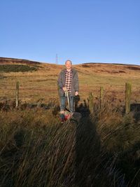 Man with dog by grass against clear sky