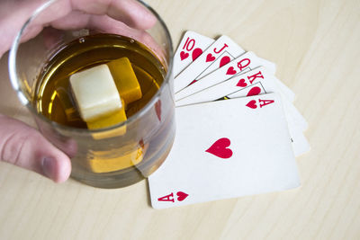 Cropped hand of man holding alcohol in glass on cards at table