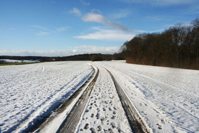 Tire tracks on snow field against sky