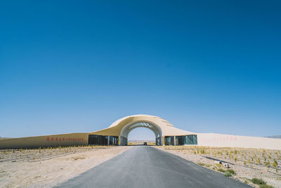 Empty road along built structures against blue sky